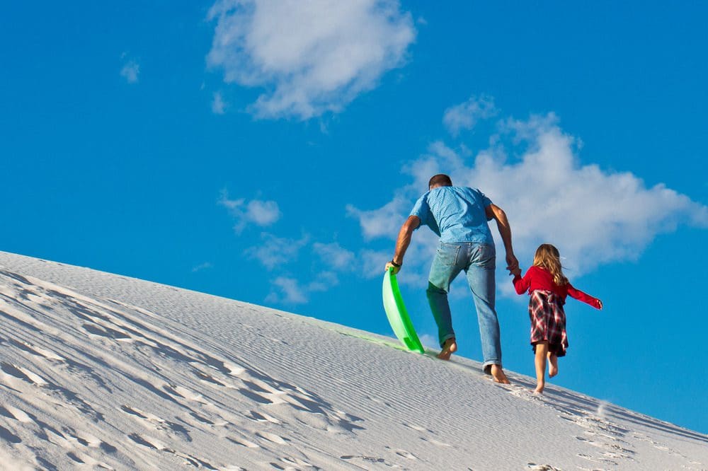 Two people climbing the dunes in white sands national park to go sledding