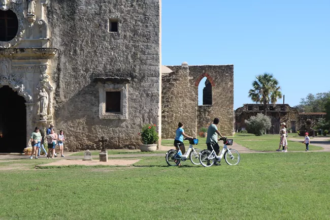 Cyclists walk their bikes in front of San Antonio Mission National Historical Park in Texas