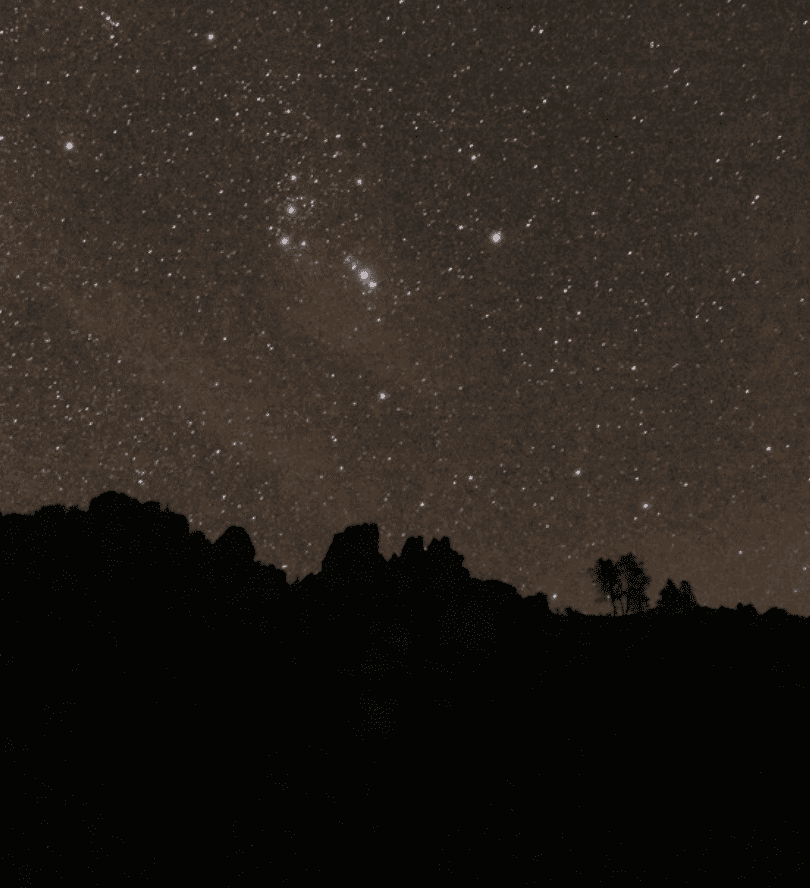 Night sky with bright stars over a mountain and treed skyline