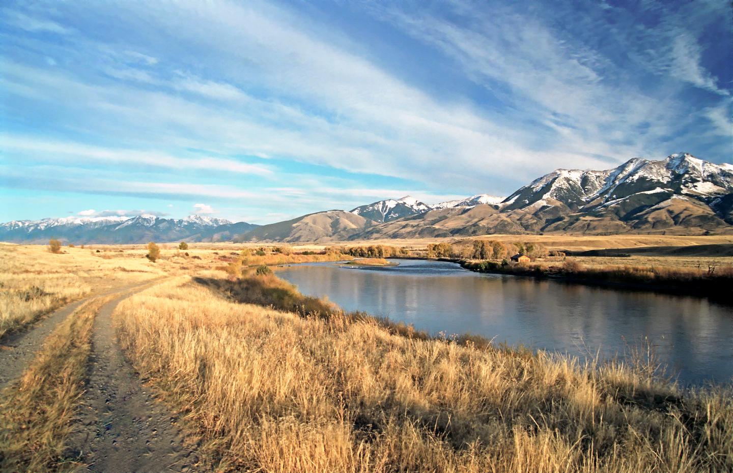 Mountain landscape with a winding river under a blue sky. Snow-capped peaks in the distance.