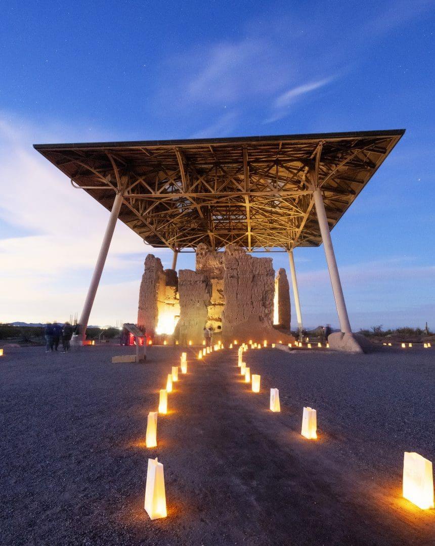Ancient ruins under a modern canopy, illuminated by lanterns at twilight.