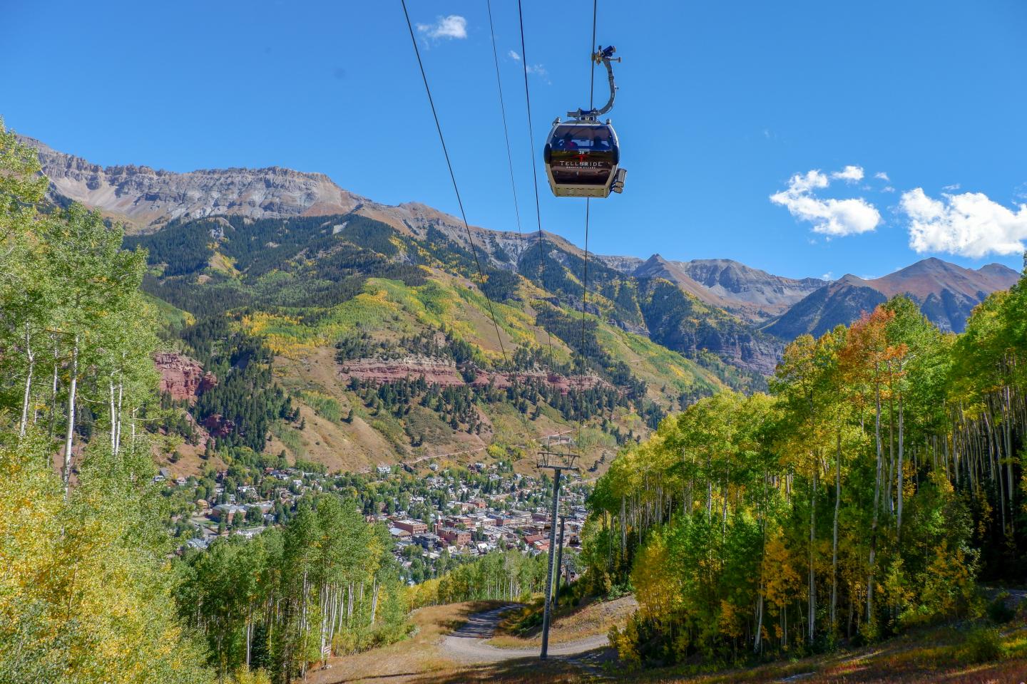 Telluride gondola car above a valley with colorful autumn trees and mountains under a clear sky.