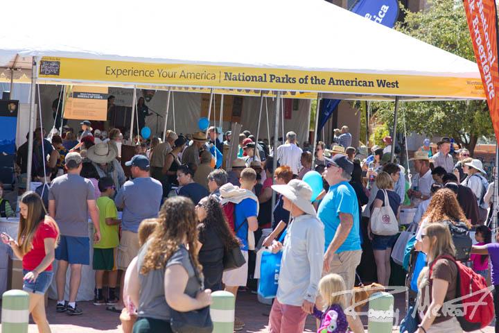Crowd gathered under a tent at an outdoor event on a sunny day at Tucson Festival of Books