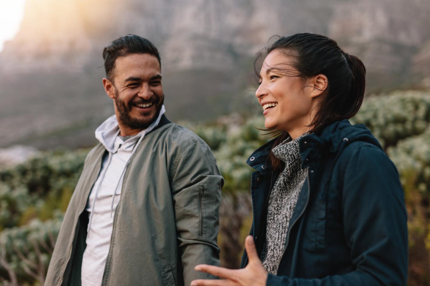 A man and woman smiling while walking outdoors in nature.