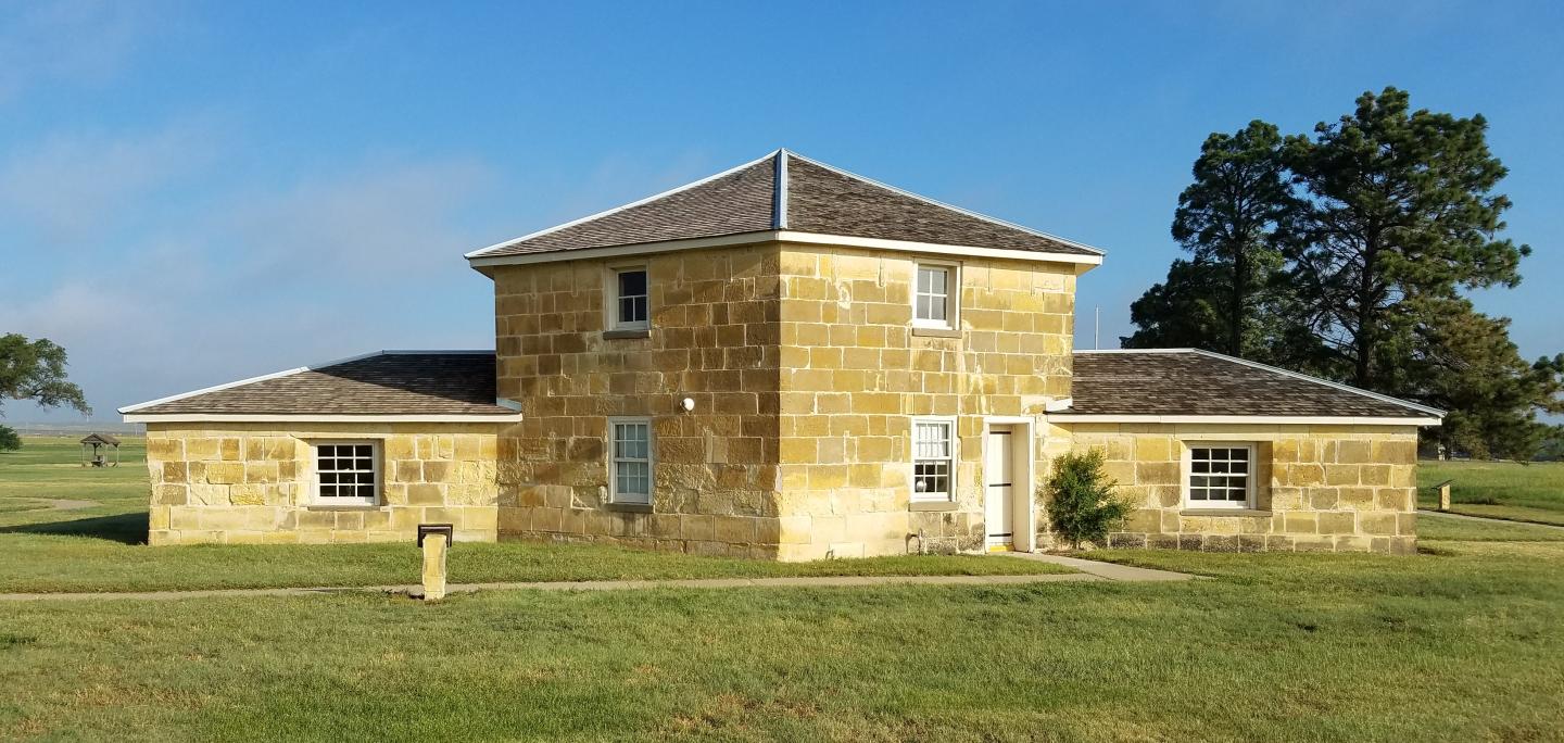 Fort Hays State Historic Site building with a central tower, surrounded by grass and trees.