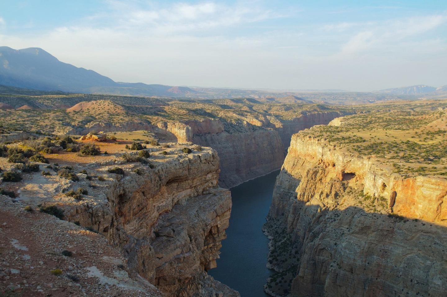 canyon with a deep blue river and sunlit cliffs under a clear sky.
