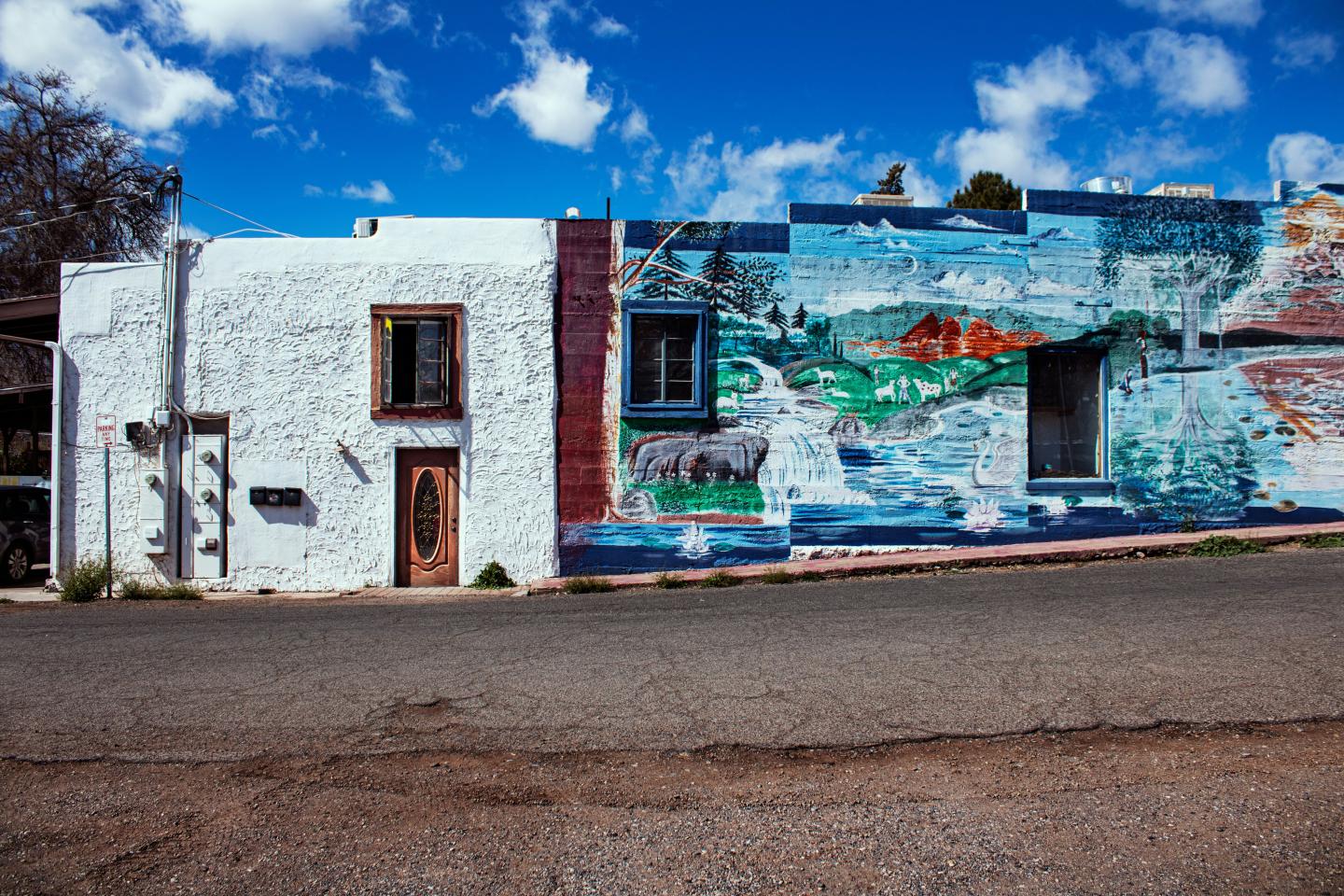 Street mural on a white building under a blue sky with clouds.
