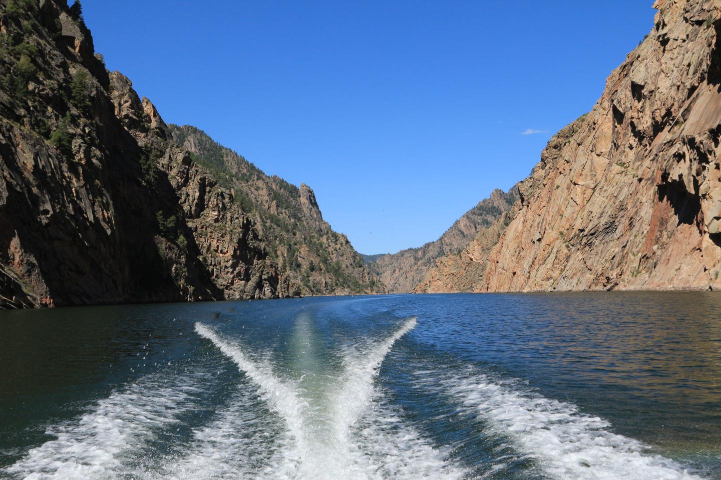 Boat wake in a narrow canyon with steep rocky walls under a clear blue sky.