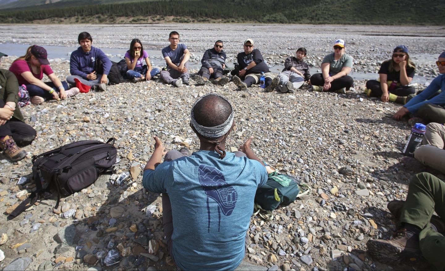 Group sitting in a circle on a rocky riverbank.