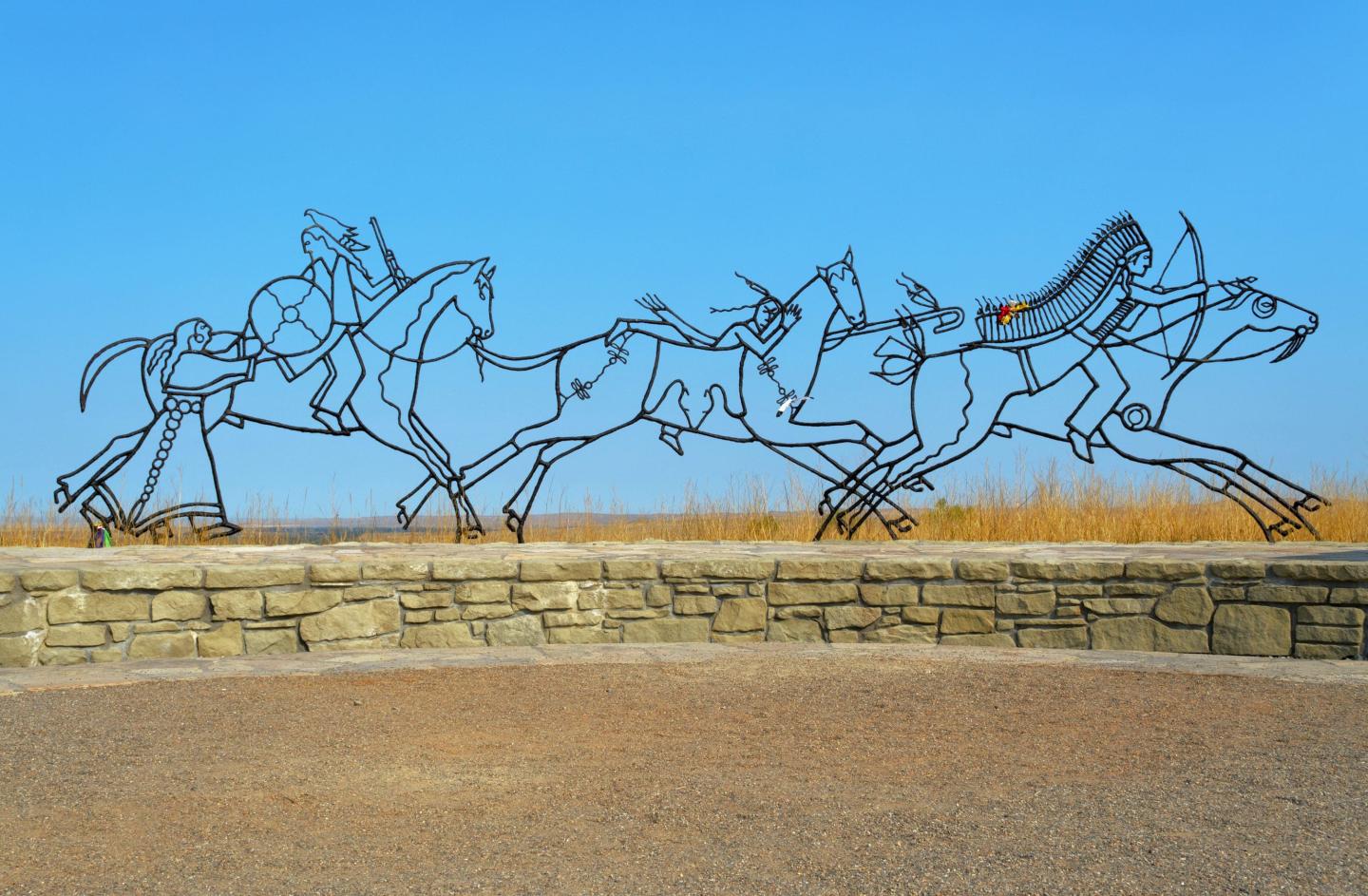 Metal sculptures of horses and riders against a clear blue sky.