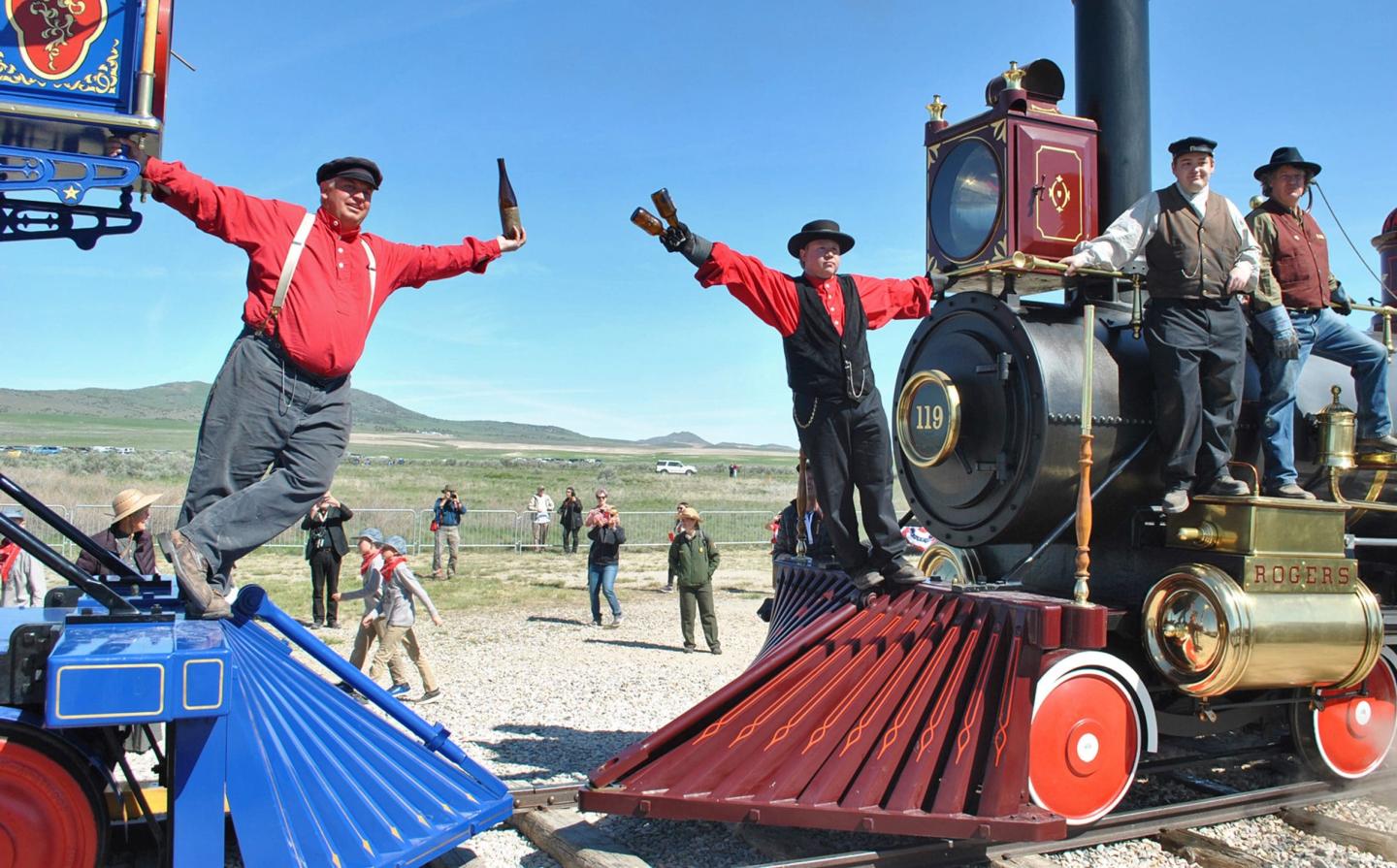Two men in period clothing celebrate atop facing trains in an open field.