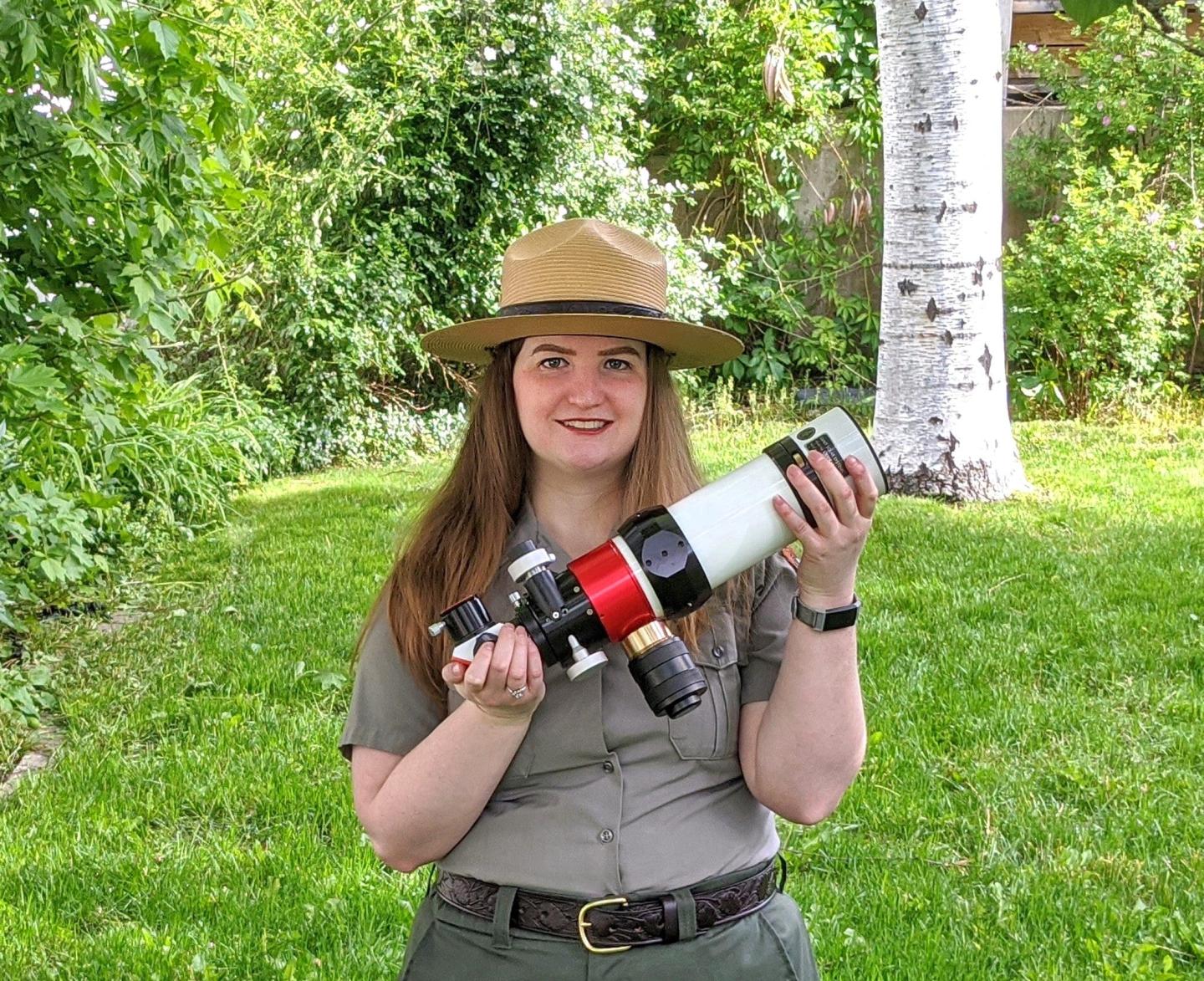 Park ranger holding a telescope outdoors.