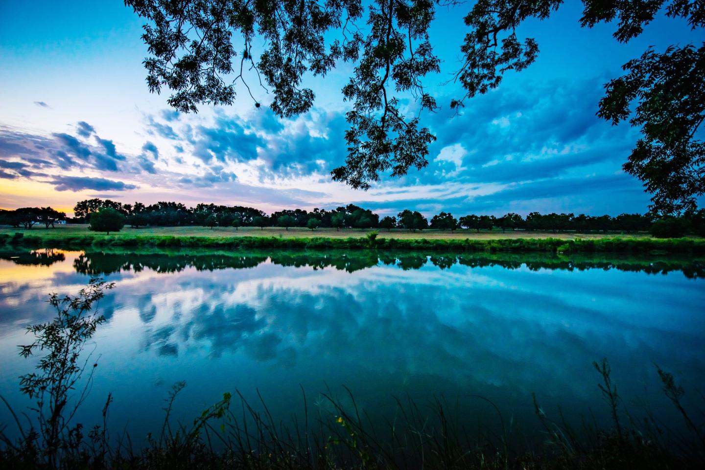 Calm lake at sunset with vibrant blue sky and clouds reflecting in the water.