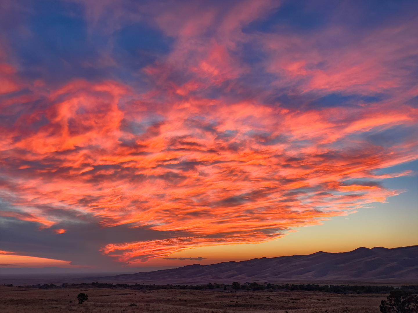Vibrant sunset with orange and pink clouds over a dark landscape.