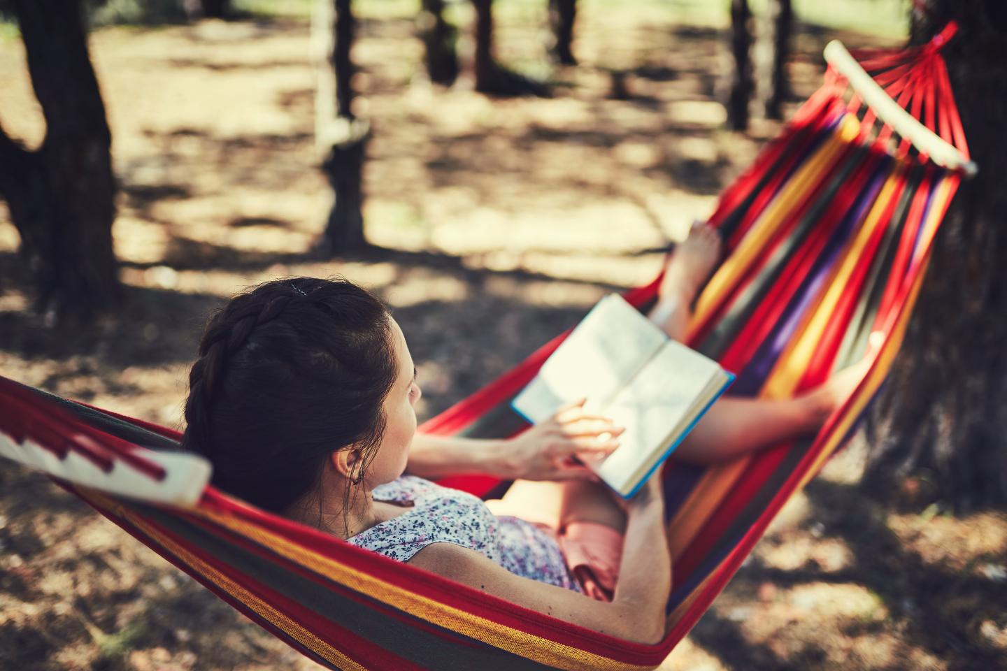 Person reading a book while reclining in a colorful hammock outdoors.
