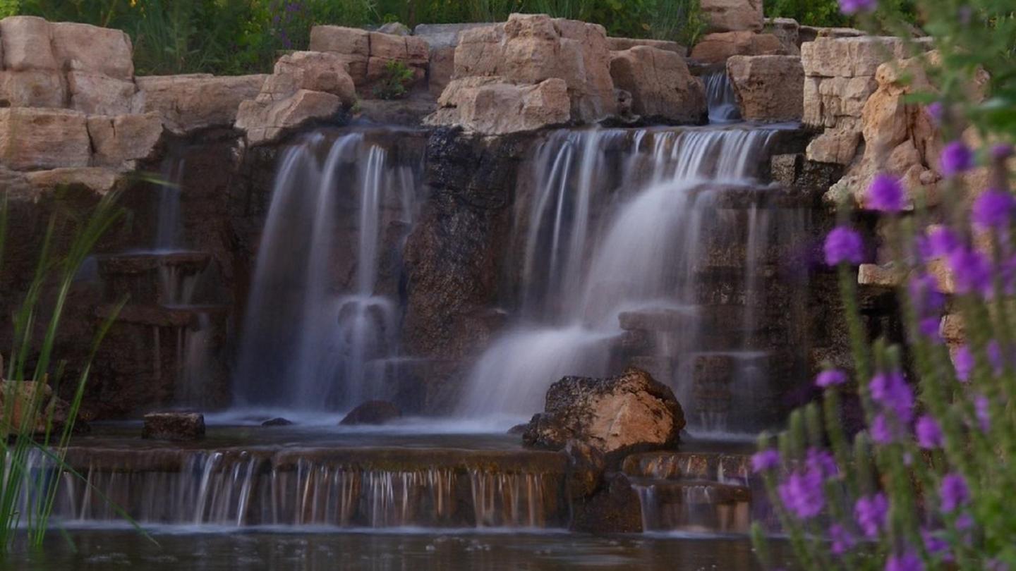 Small waterfall at Ponca state park with rocks and purple flowers at dusk.