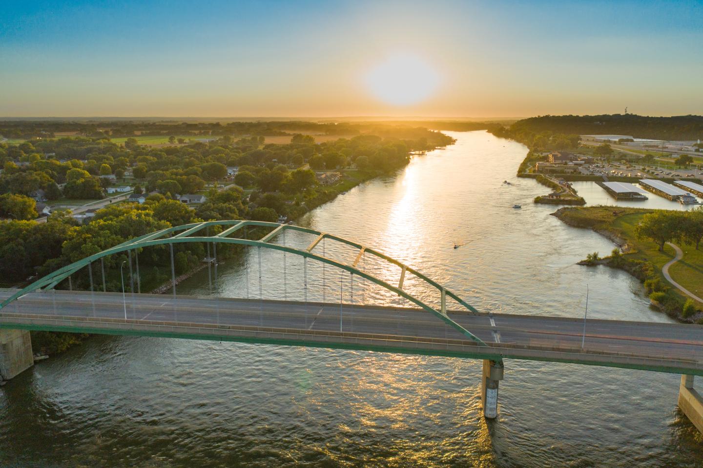 Sunset over the Missouri River with arch bridge, surrounded by trees and distant buildings.