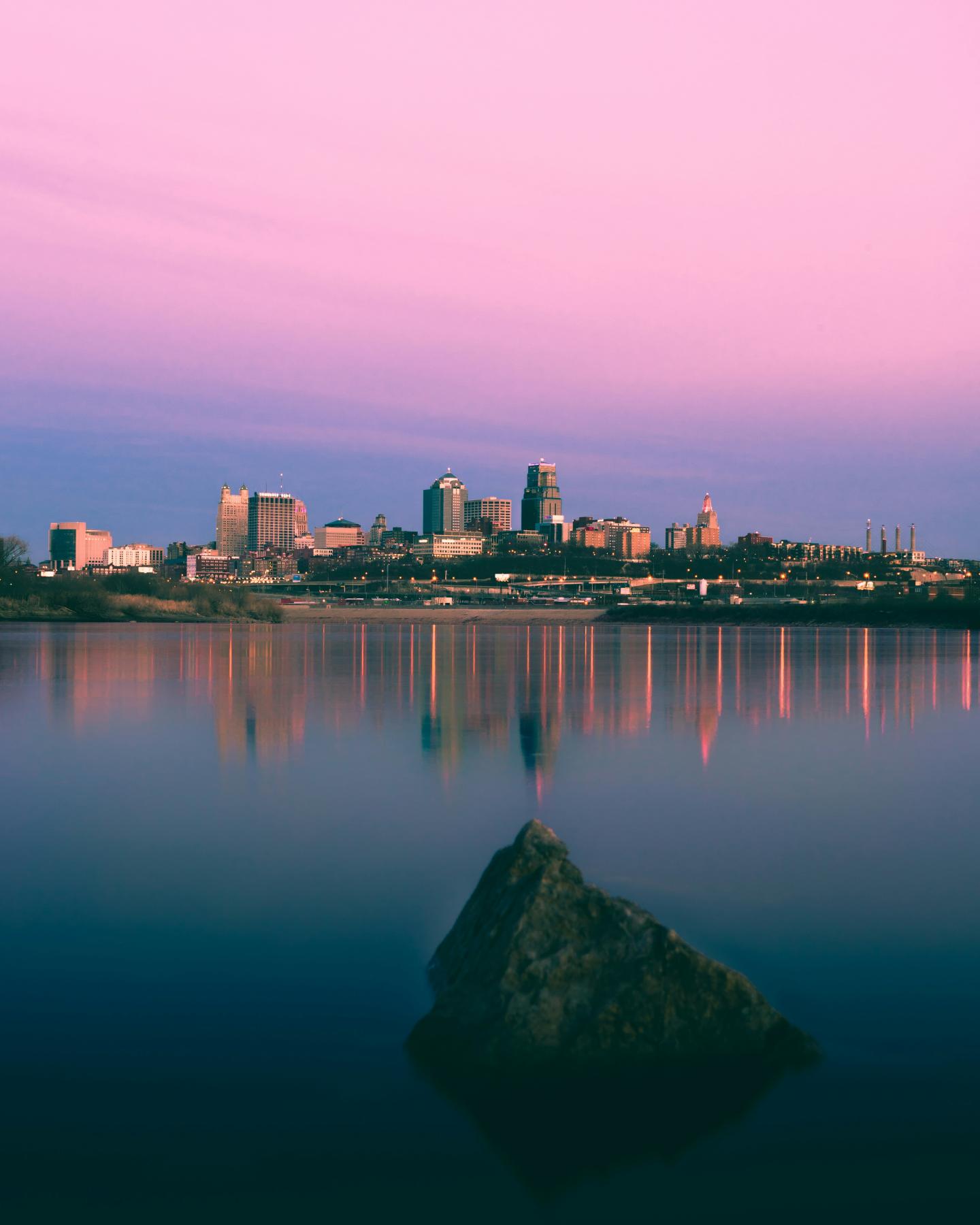 Kansas City skyline reflected in calm water at sunset.