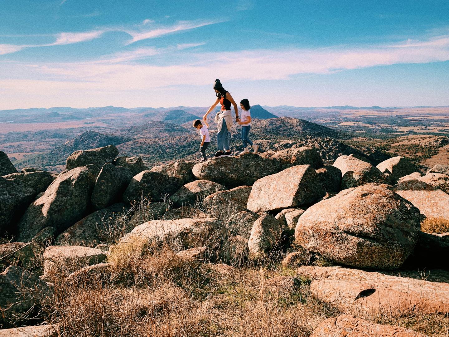 Family enjoying view from rocky hilltop overlooking vast landscape.