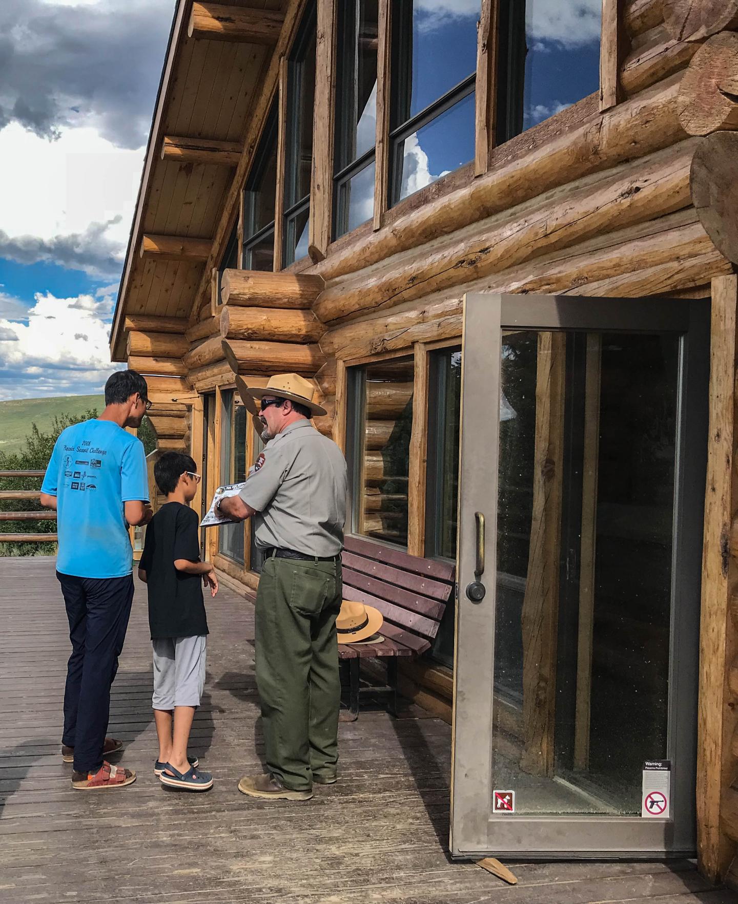 Three people outside a visitor center, one in a park ranger outfit, on a cloudy day.