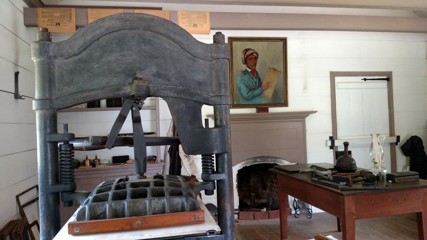 A historic printing press in a room with a portrait and fireplace.