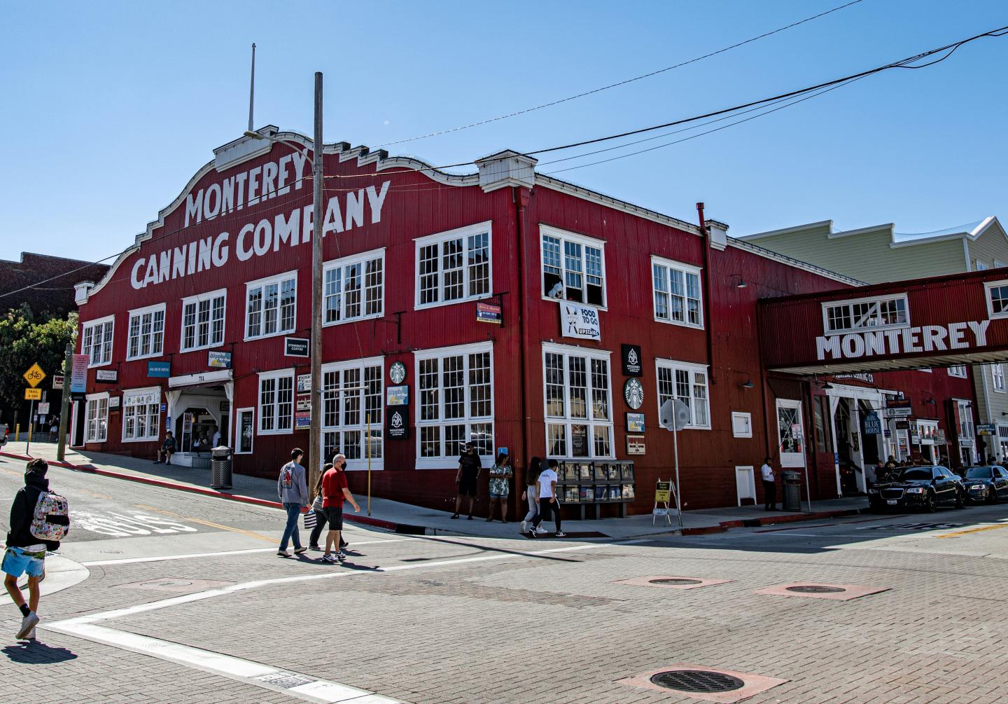 Red building on a street corner, people walking, clear blue sky.