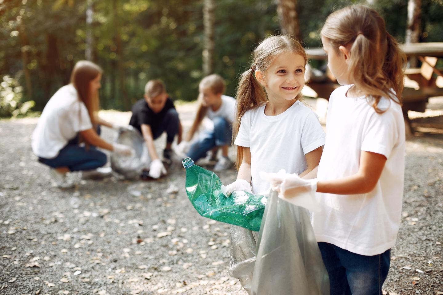 Children cleaning a park, two girls in the foreground smiling.