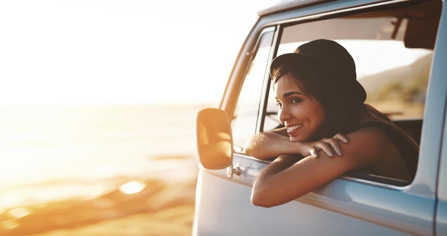 Woman smiling, leaning out of van window, ocean background.