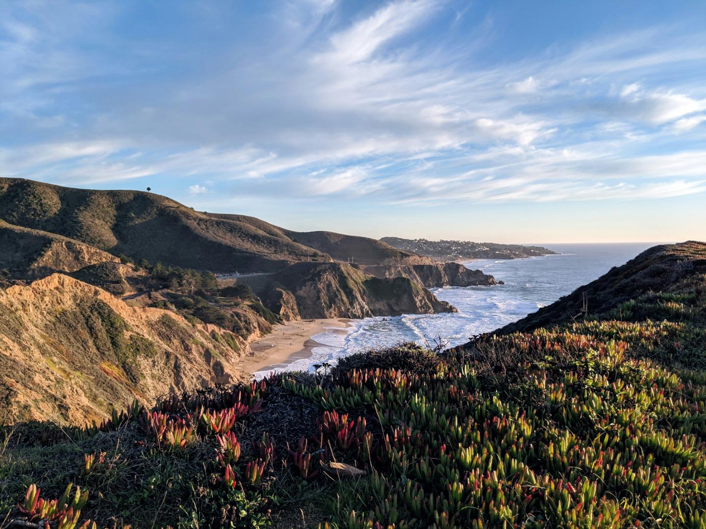 Coastal cliffs and ocean under a blue sky with light clouds.