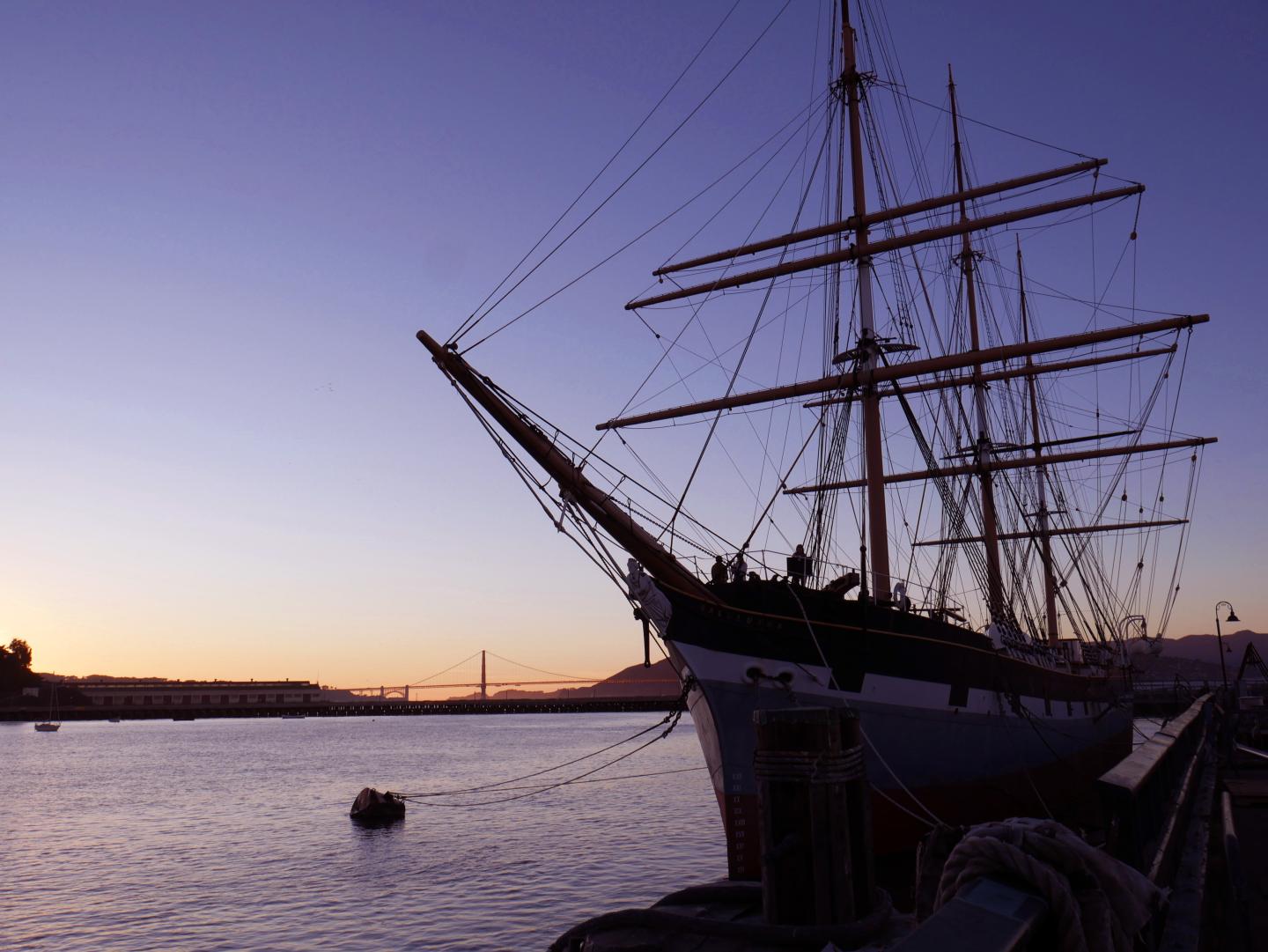 Balcutha ship docked at sunset with a calm sea and silhouetted sky.
