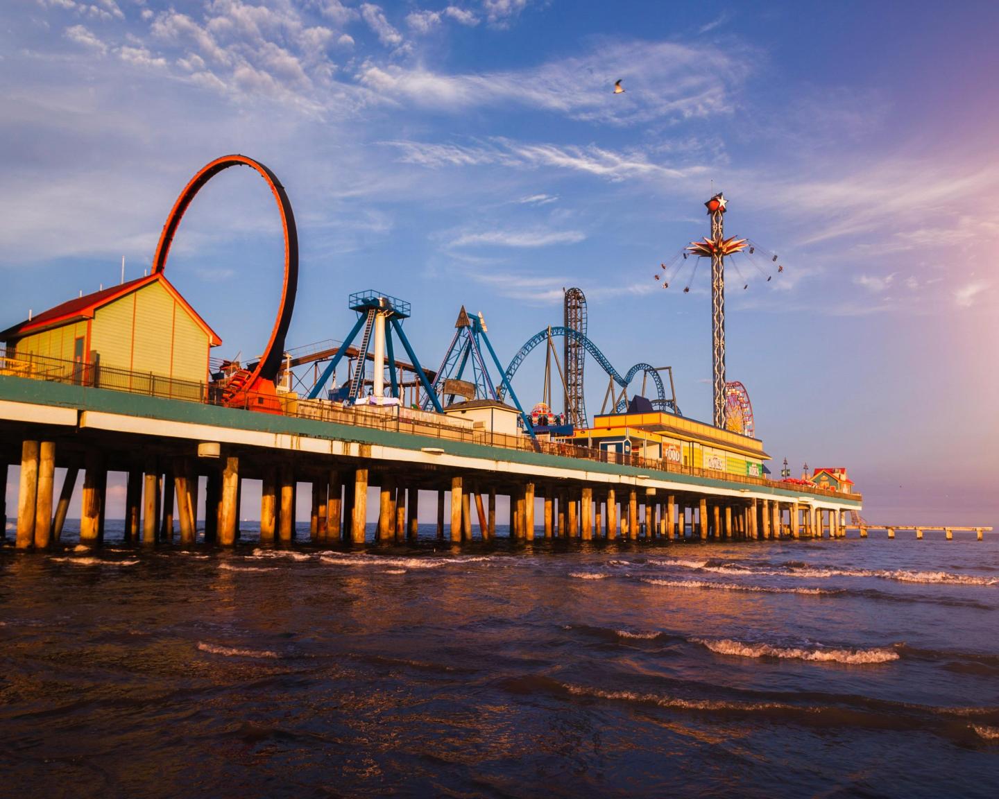 Amusement park pier at sunset over ocean waves.