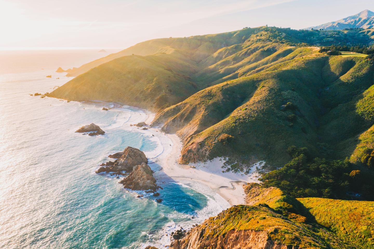 Big Sur landscape with green hills, rocky shore, and blue sea at sunset.