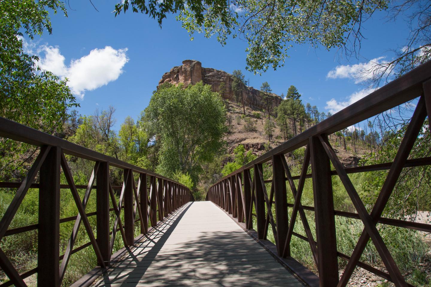 Bridge leading toward a rocky hill under a blue sky with clouds.