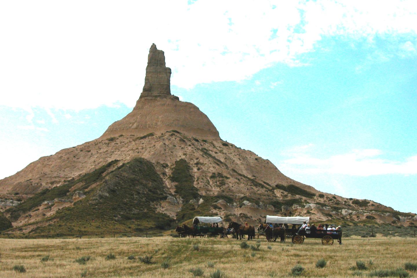 Chimney Rock with covered wagons beneath a blue sky.