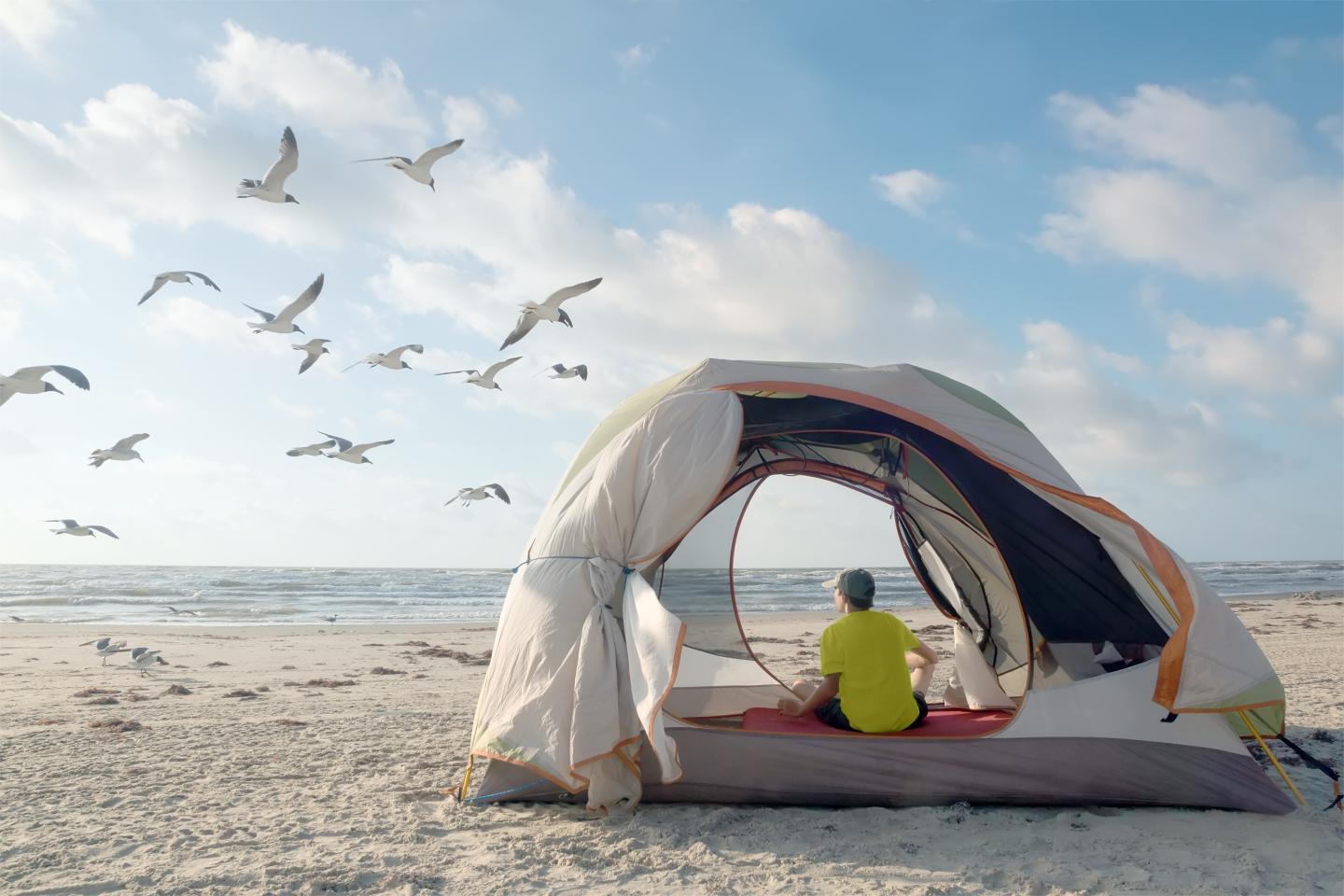 Tent on Padre Island with person sitting, watching seagulls and ocean.
