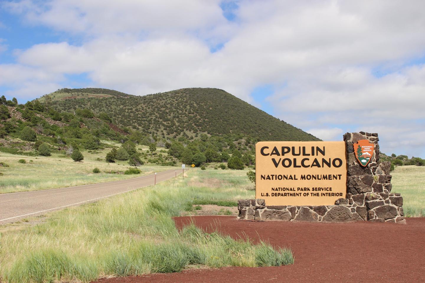 Capulin Volcano sign in grassy landscape with distant green hill.