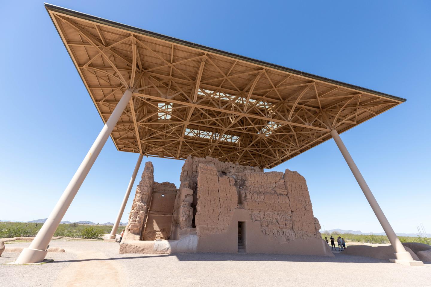 Casa Grande ruins under a large protective metal canopy, clear blue sky.