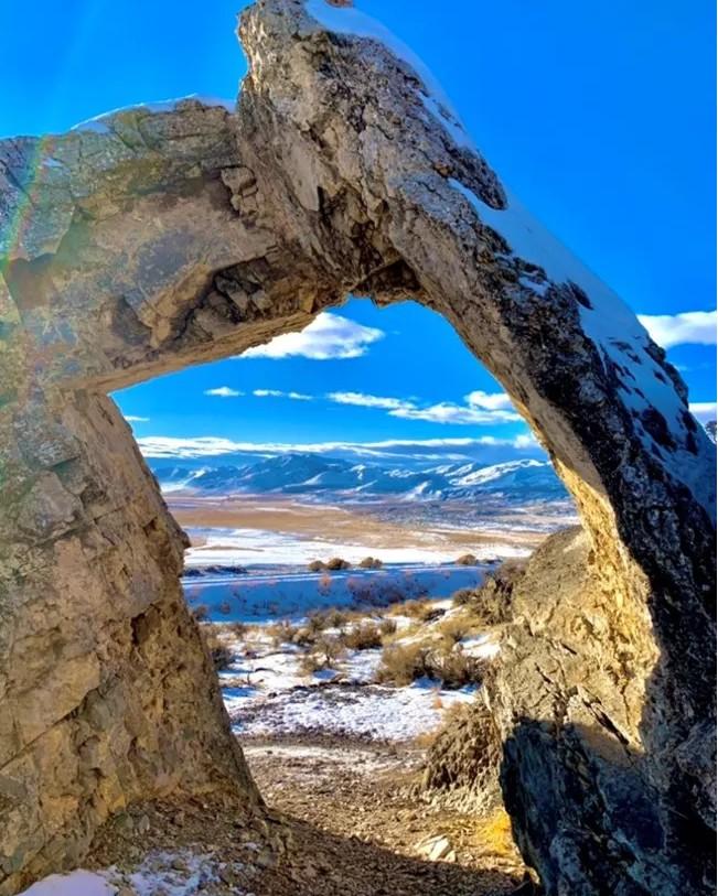 Chinese arch framing a snowy mountain landscape under a clear blue sky.