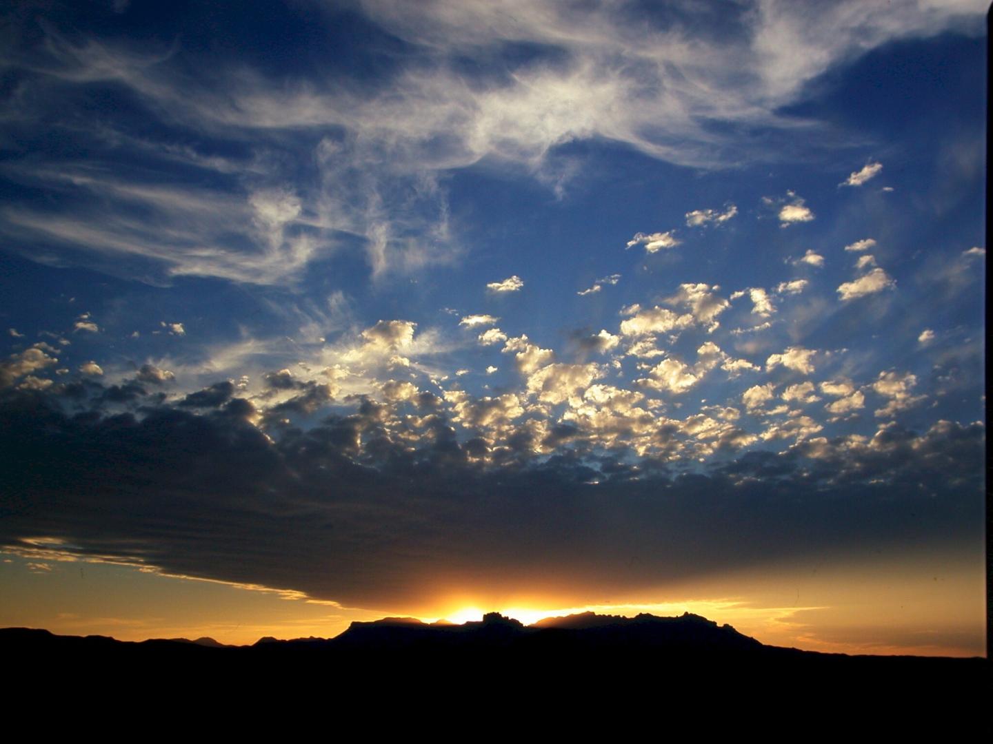 Sunset behind silhouetted Chisos mountains, with dramatic clouds in a darkening sky.