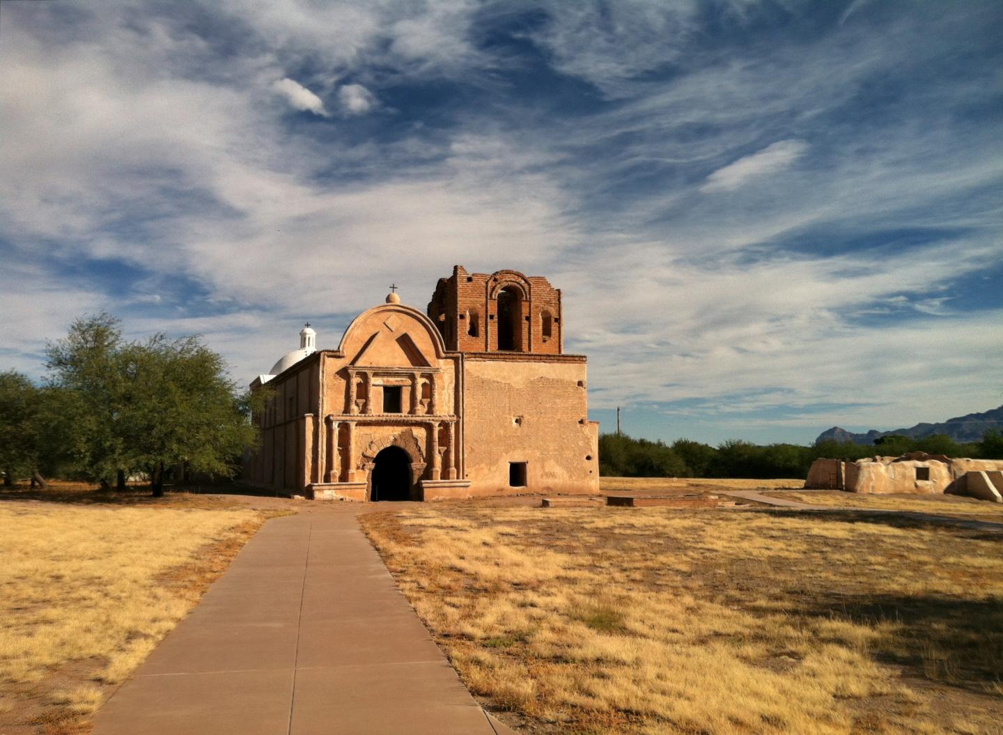 Historic adobe church under a blue sky with clouds.
