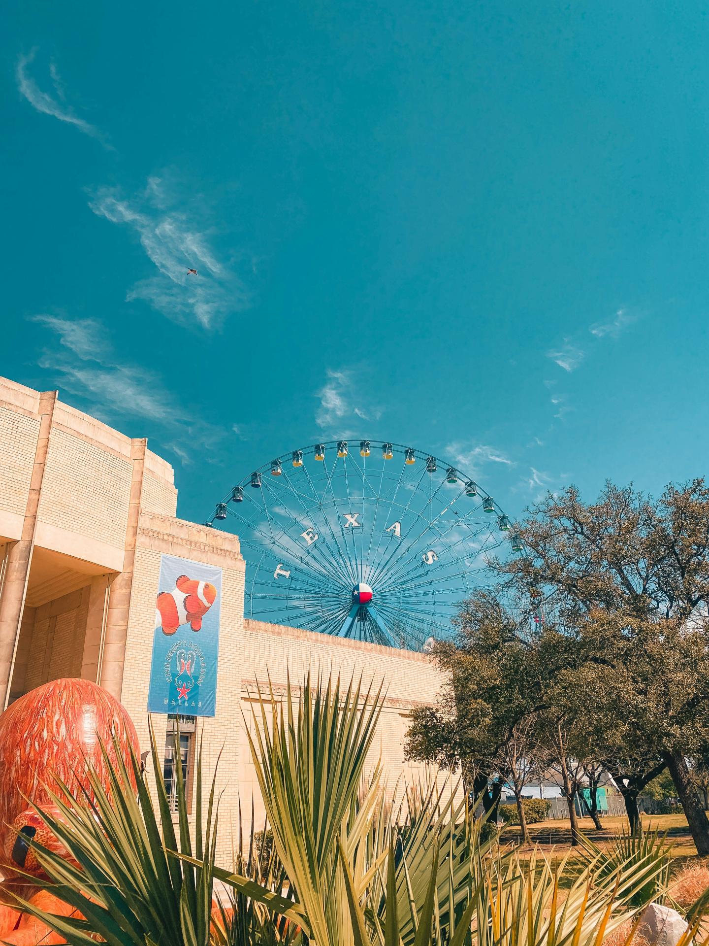 Ferris wheel behind a building, with clear blue sky and trees.
