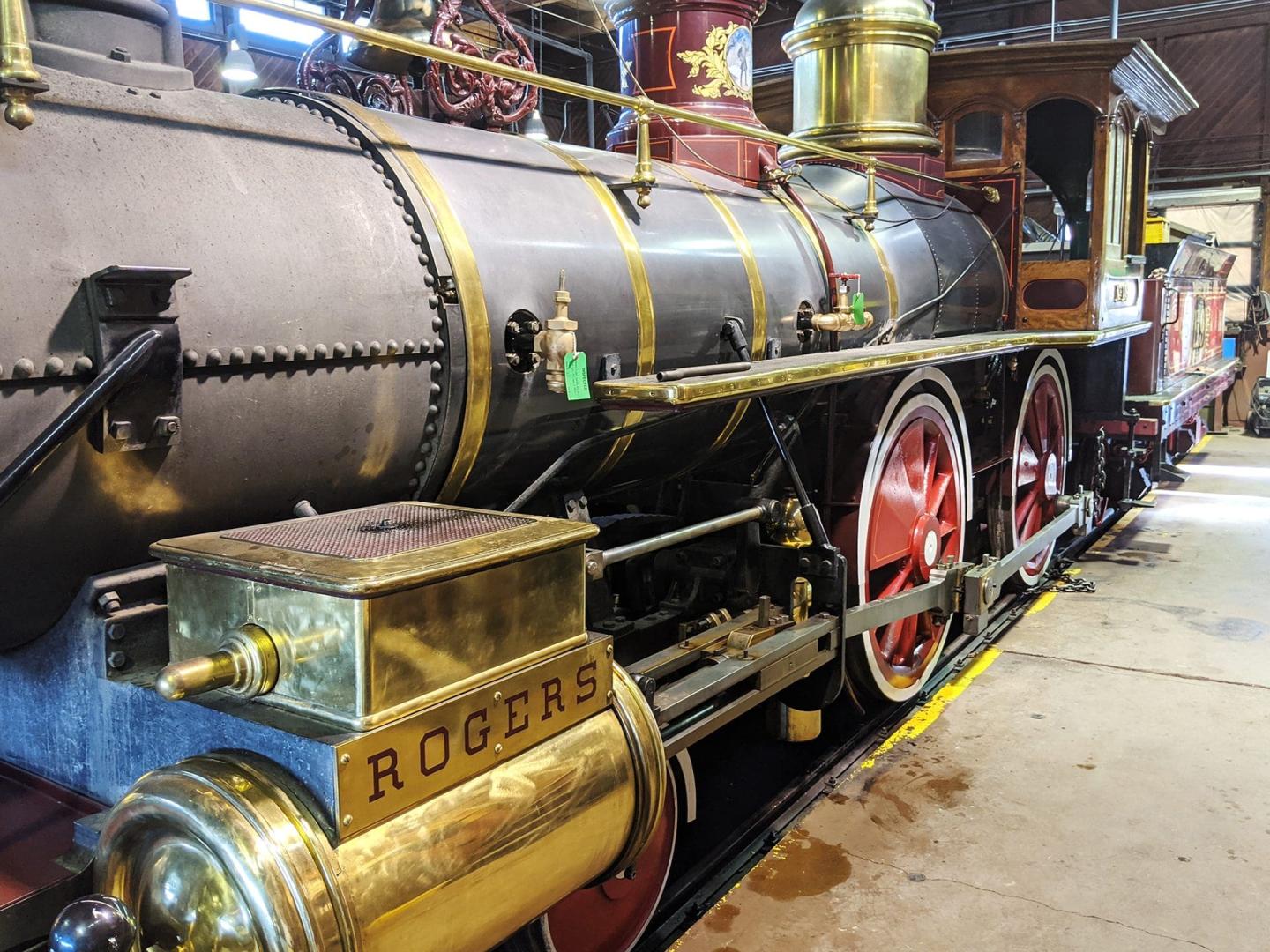 Steam locomotive with red wheels and brass accents in a train shed.