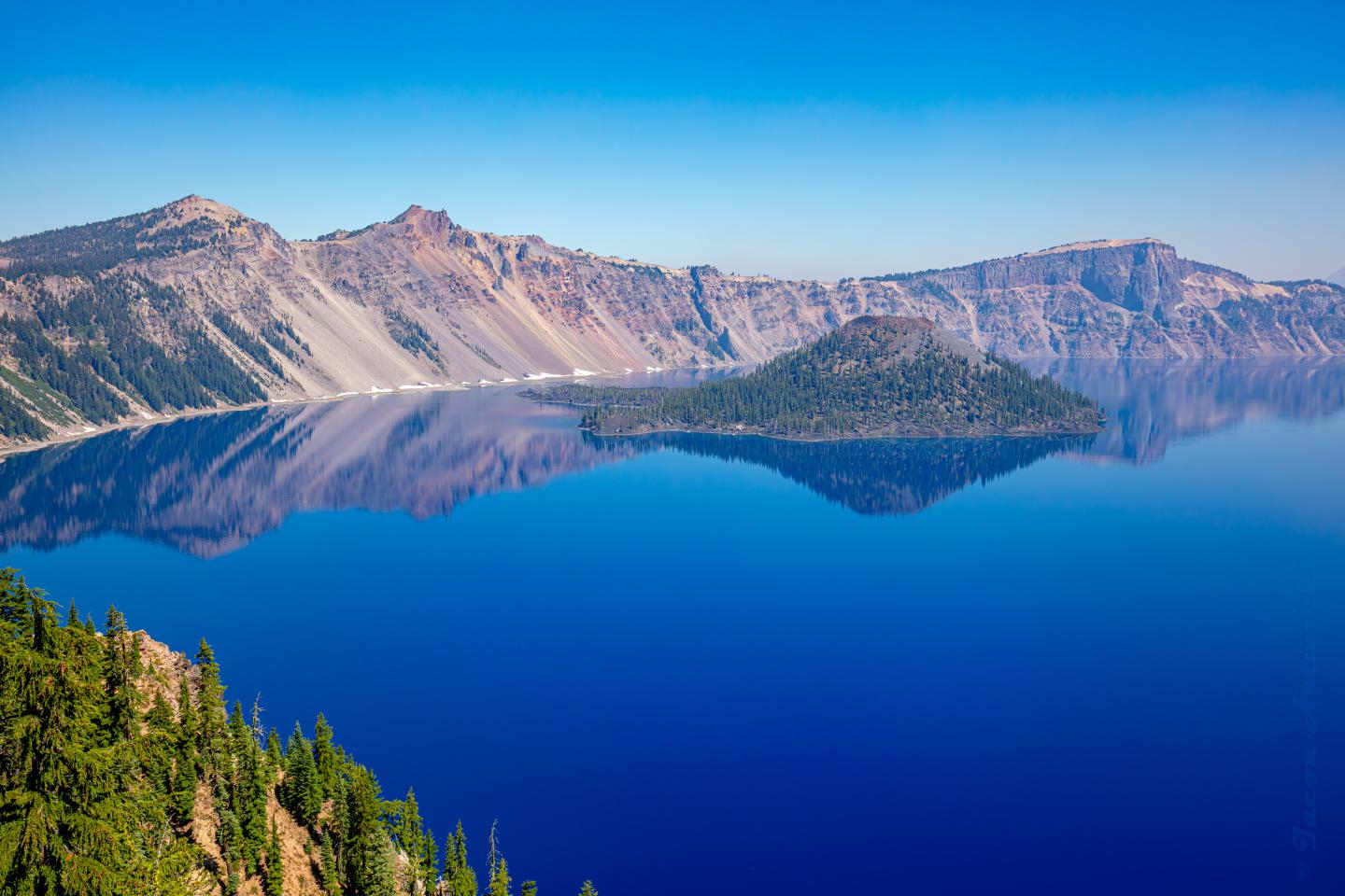 Crater Lake's azure waters surrounded by rugged mountain range under a clear blue sky.