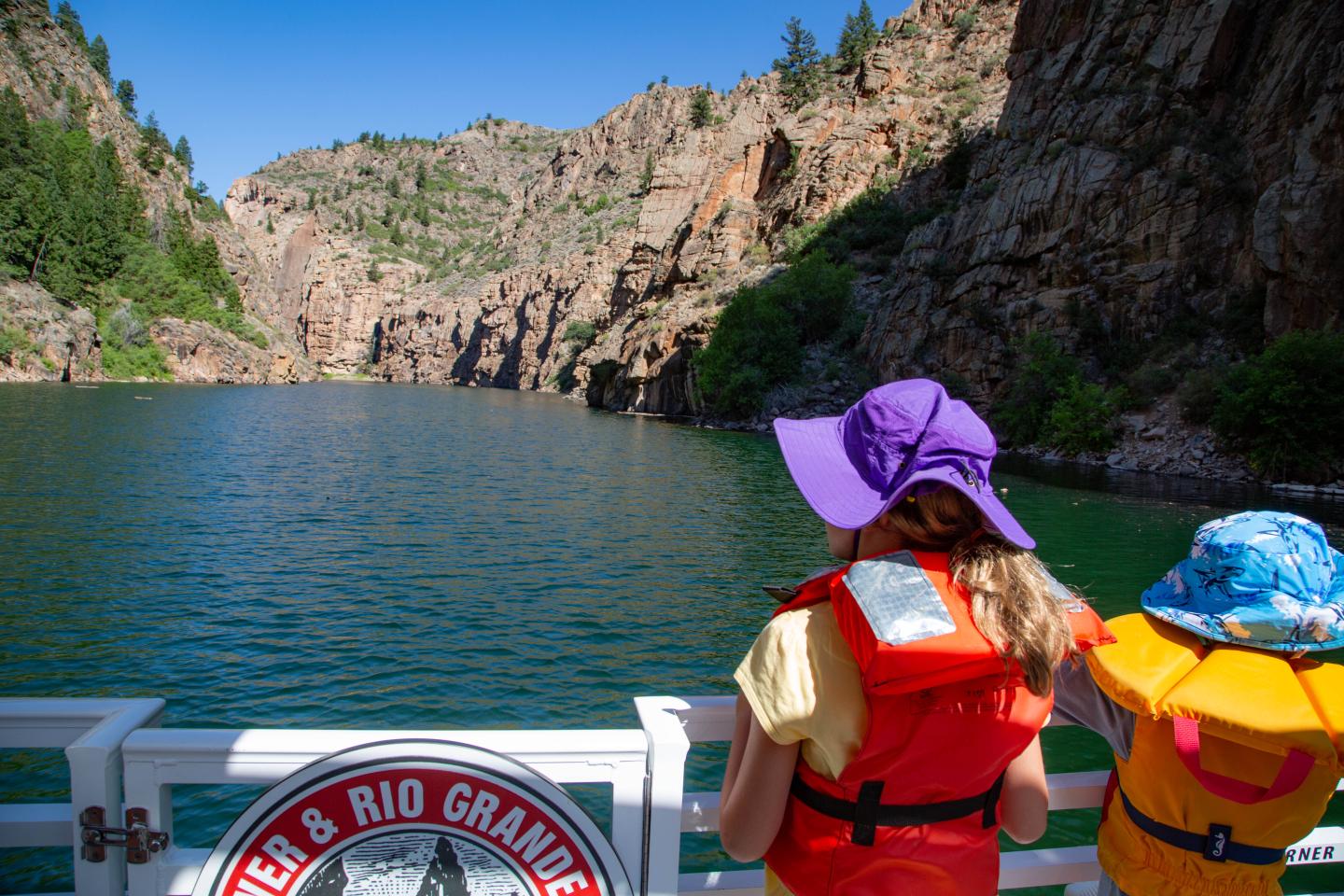 Two children in life vests admire a scenic river canyon.