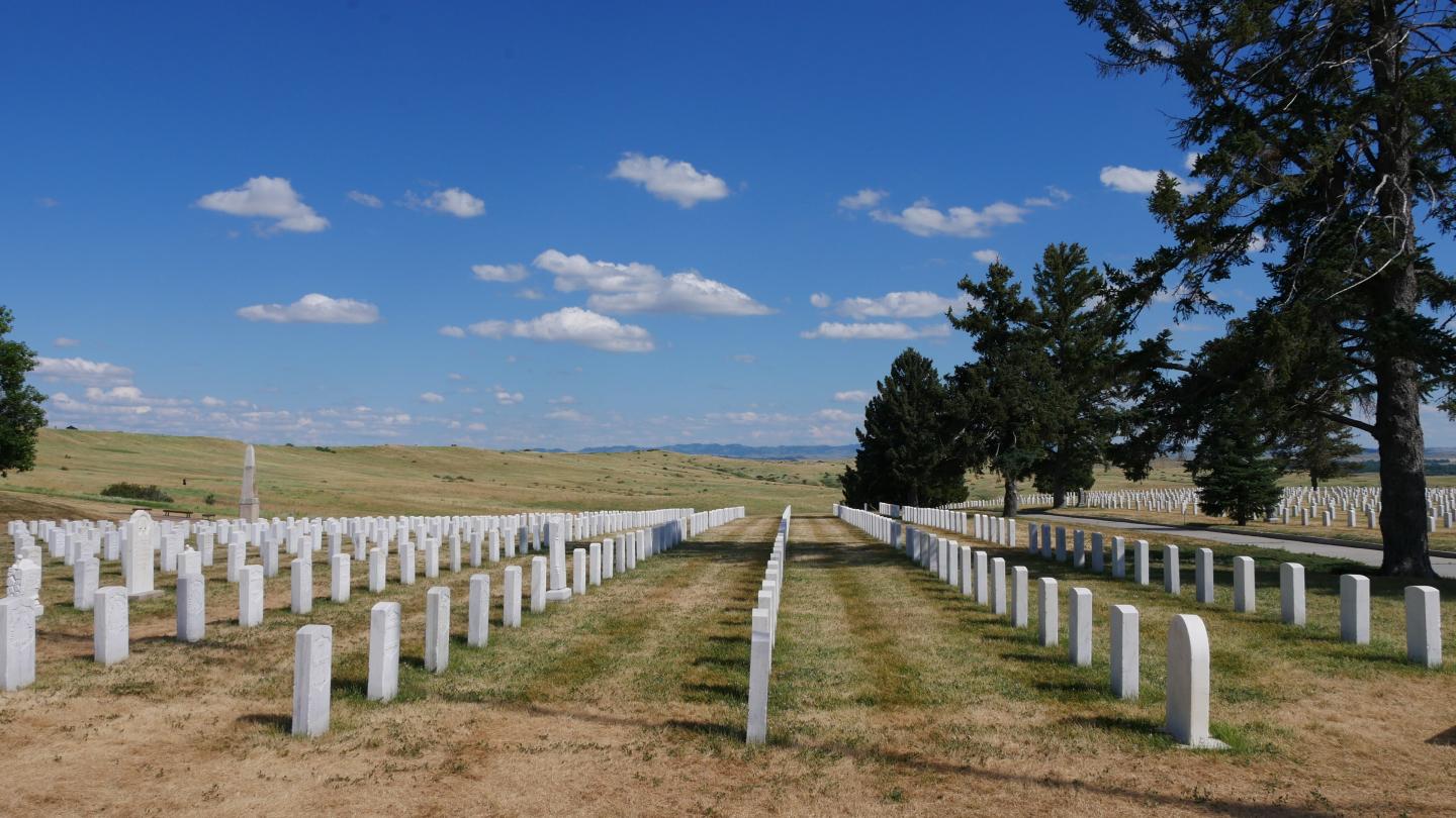 Rows of white gravestones in Custer National Cemetery under a blue sky.
