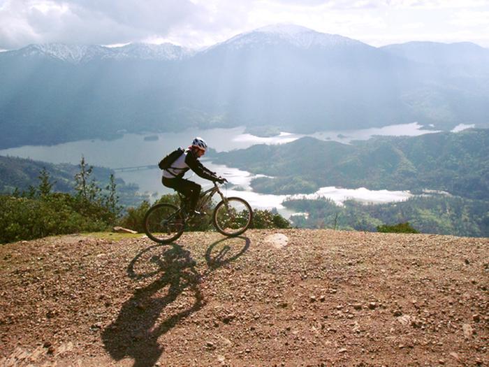 Cyclist on mountain trail with scenic lake and mountains.