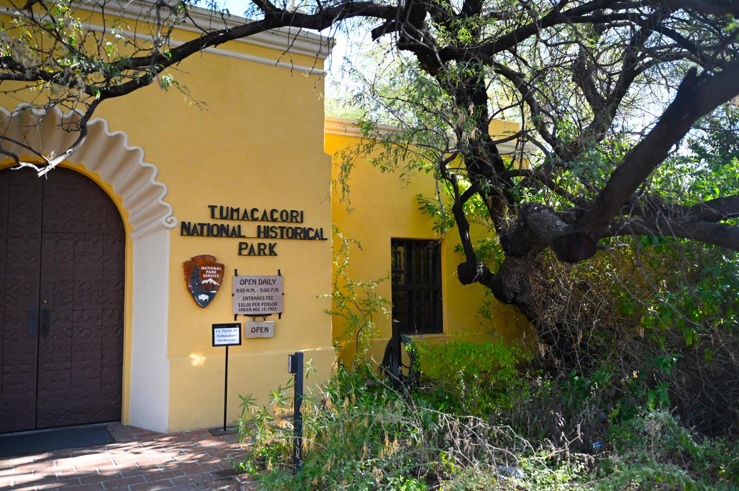 Yellow visitor centre building with arched doorway, tree in front, and signage for historical park.