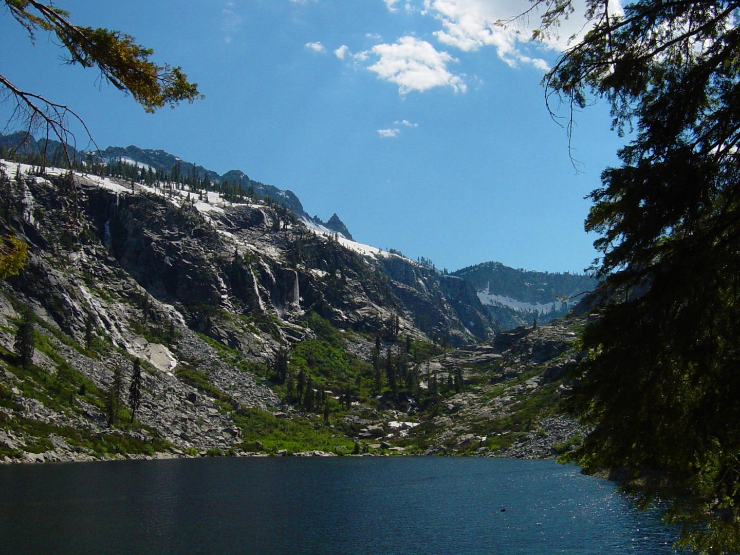 Mountain lake beneath a clear blue sky, surrounded by rocky peaks and trees.