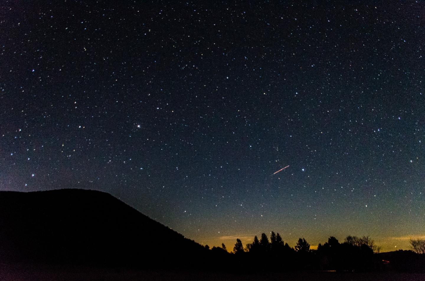 Starry night sky over a silhouetted landscape.