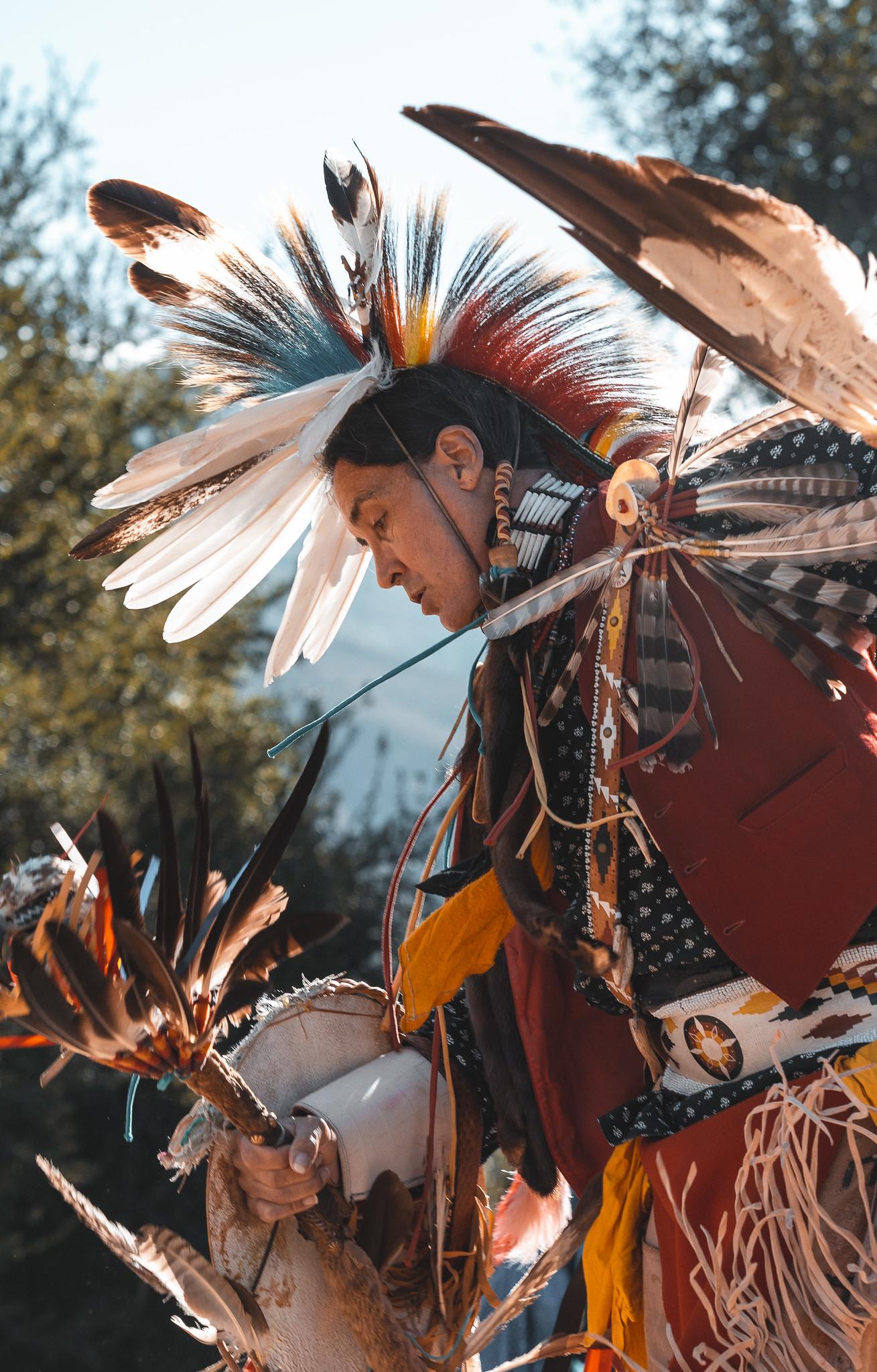 Person dressed in traditional attire with feathered headdress outdoors.